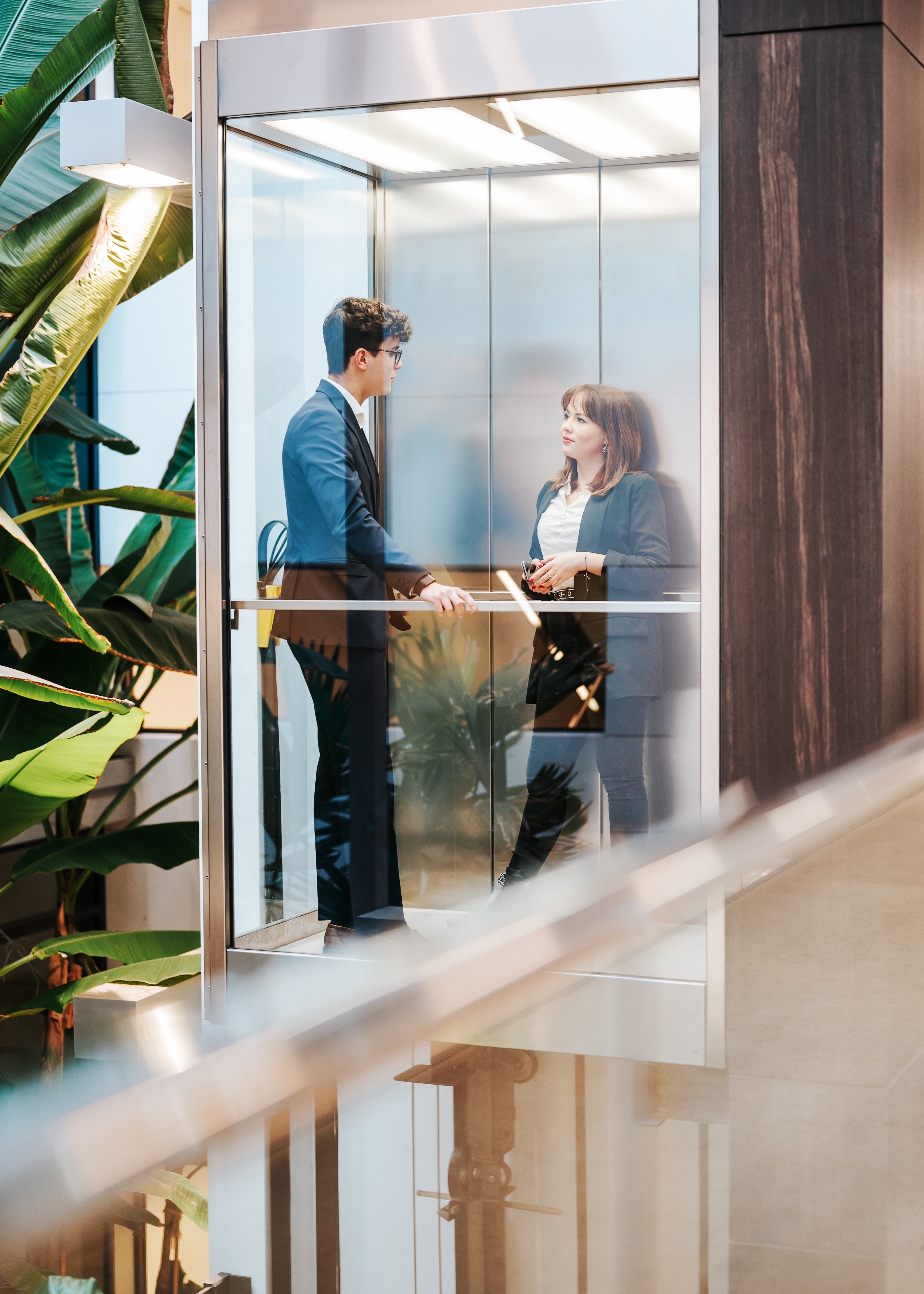 Zwei Mitarbeitende der Baaderbank in einem verglasten Aufzug im modernen Bürogebäude.